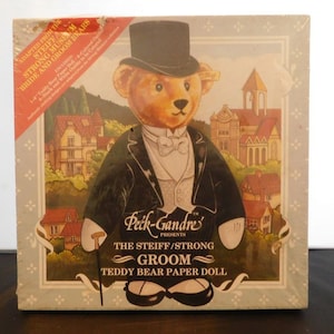 May include: A paper doll set featuring a teddy bear dressed in a black tuxedo with a top hat and a white bow tie. The box features a colorful illustration of the bear in a town setting. The text on the box reads "Peck-Gandre's Presents The Steiff/Strong Groom Teddy Bear Paper Doll".