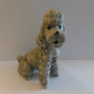 May include: A gray ceramic poodle figurine with a curly tail and a sitting pose.
