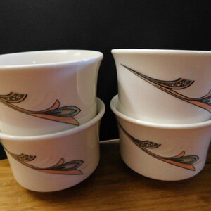 May include: Set of four white ceramic coffee mugs with a delicate floral design in shades of brown, pink, and green. The mugs are stacked in pairs.