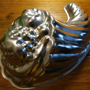 May include: A silver metal cornucopia-shaped baking pan with a fluted design. The pan is designed to hold a cornucopia-shaped cake or dessert.