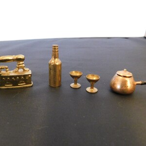 May include: A set of miniature gold-toned metal objects, including a bottle, two wine glasses, an iron, and a copper pot with a black handle.