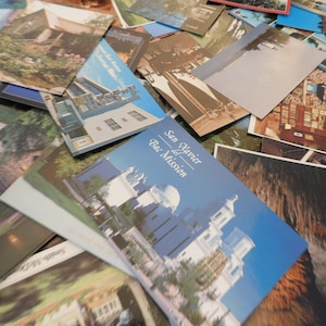 May include: A stack of vintage postcards featuring various locations and scenes. The top postcard shows a building with the text "San Xavier del Bac Mission".