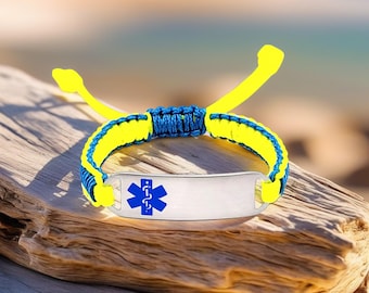 May include: A medical alert bracelet with a silver ID plate and a blue Star of Life symbol. The bracelet features a woven design with blue and yellow cords, and adjustable yellow cords for closure. The bracelet is displayed on a piece of driftwood.