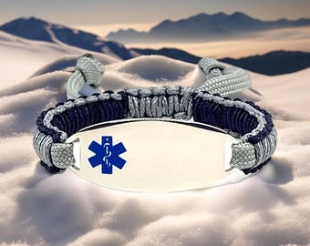 May include: A medical ID bracelet with a silver metal plate and a blue Star of Life symbol. The bracelet features a woven design in navy blue and gray, with a gray clasp. The background shows a snowy landscape with mountains.