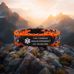 May include: Orange and grey paracord bracelet with a black clasp. The black plate has the text "TYPE 1 DIABETES, INSULIN DEPENDENT, ICE: 123-456-7890" and a white medical symbol. The bracelet is on a rocky surface.