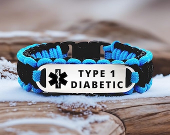 May include: A black and blue paracord bracelet with a silver plate. The plate has a medical symbol and the words "TYPE 1 DIABETIC" in black text. The bracelet is on a wooden surface with snow.