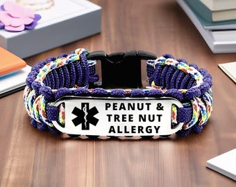 May include: A blue paracord bracelet with a black buckle and a metal plate. The plate has a medical symbol and the text "PEANUT & TREE NUT ALLERGY". The bracelet has a colorful woven design.
