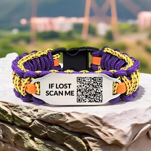 Puede incluir: Una vibrante pulsera de paracord en morado, amarillo y naranja, con una hebilla negra. Una etiqueta plateada muestra el texto "IF LOST SCAN ME" y un código QR. Diseñada para actividades al aire libre.