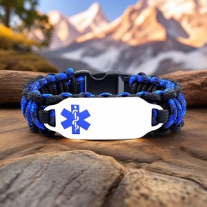 May include: A black and blue paracord bracelet with a white metal plate featuring a blue medical symbol. The bracelet is secured with a black plastic clasp. The background shows a mountain range.