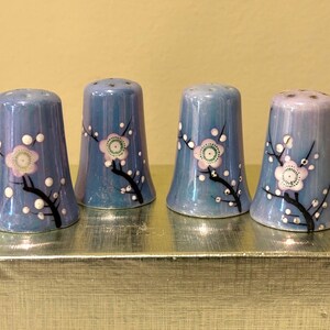 May include: Four blue ceramic salt and pepper shakers with a floral design. Each shaker has a white and pink flower with a black stem and white dots.