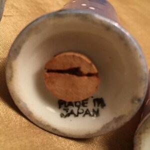 May include: Close-up of the bottom of a white ceramic salt or pepper shaker with a cork stopper. The shaker has a blue and white polka dot design and says "Made in Japan" on the bottom.