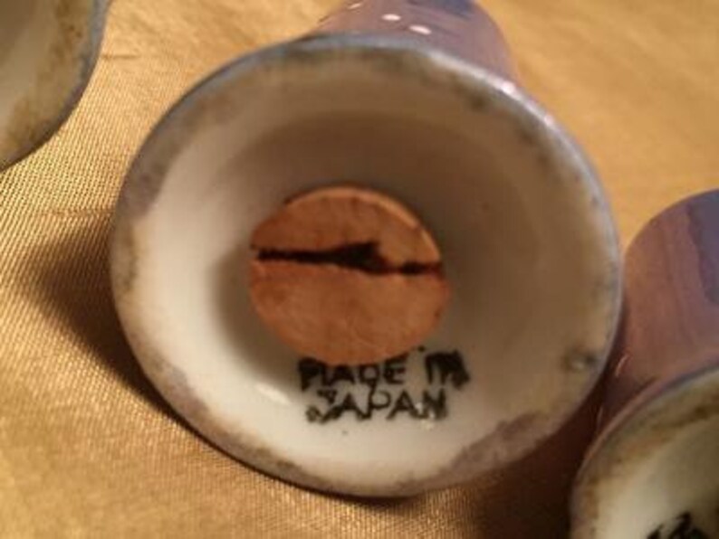 May include: Close-up of the bottom of a white ceramic salt or pepper shaker with a cork stopper. The shaker has a blue and white polka dot design and says "Made in Japan" on the bottom.