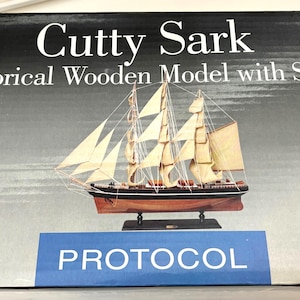 May include: A wooden model of the Cutty Sark, a historical sailing ship, with a stand. The model is on a box with the words "Cutty Sark Historical Wooden Model with Stand" and "PROTOCOL" printed on it.