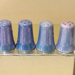 May include: Four blue ceramic thimbles with white and brown speckles. The thimbles are lined up on a gold surface.