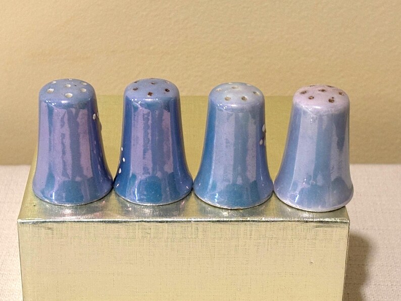 May include: Four blue ceramic thimbles with white and brown speckles. The thimbles are lined up on a gold surface.