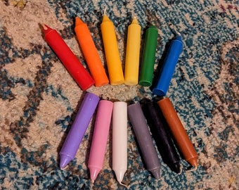 May include: A set of 12 colorful candles arranged in a circle. The candles are all the same size and shape, and they are arranged in a rainbow pattern. The candles are on a light brown and blue patterned surface.
