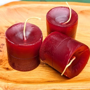 Puede incluir: Tres velas rojas en forma de pilar con mechas blancas sobre una superficie de madera.