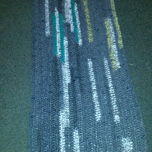 May include: A gray woven rug with white, green, and yellow stripes. The rug has a textured surface and is made of a woven material.