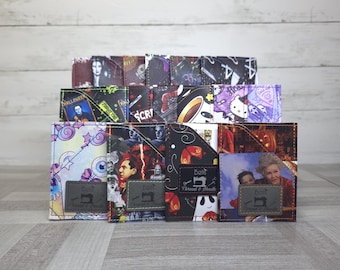May include: A collection of rectangular fabric card holders featuring various horror and pop culture prints. Each holder has a diagonal pocket and a small grey rectangular label with the text Bells Thread & Needle and a sewing machine icon.
