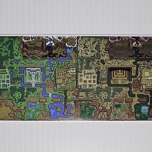 May include: A detailed map print featuring a pixelated design with green, brown, and blue hues. The map depicts a complex layout of pathways, structures, and natural elements, reminiscent of a video game world. The print is rectangular and set against a white background.