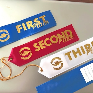 Puede incluir: Cuatro cintas de satén en azul, rojo y blanco, con letras doradas y un emblema dorado. Las cintas dicen "FIRST Place", "SECOND Place" y "THIRD Place". Una cinta azul tiene una etiqueta en blanco.