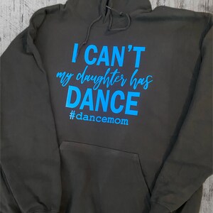 May include: A dark grey hooded sweatshirt with the text "I CAN'T my daughter has DANCE #dancemom" in blue.