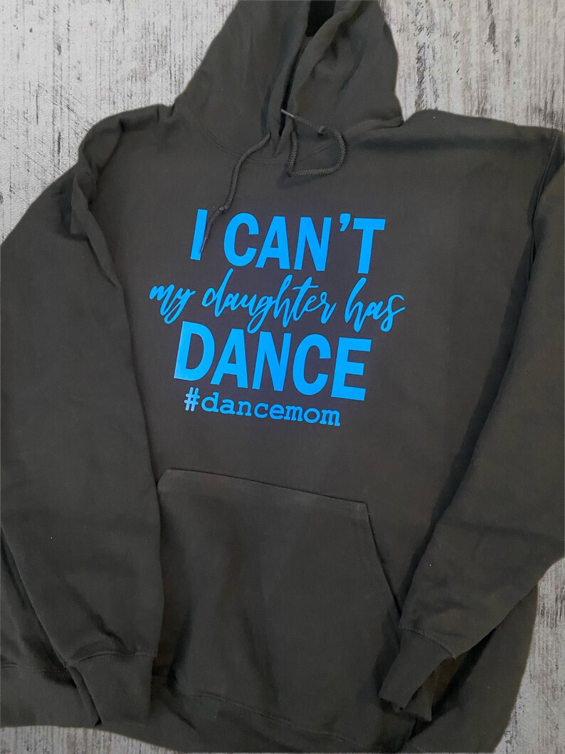 May include: A dark grey hooded sweatshirt with the text "I CAN'T my daughter has DANCE #dancemom" in blue.