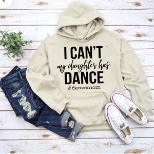 May include: A beige hoodie with a black graphic that says "I can't my daughter has dance #dancemom".