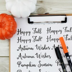 May include: A printable worksheet with the words "Happy Fall", "Autumn Wishes", "Pumpkin Season", "Give Thanks", "Leaves", and "Colors" written in cursive. The worksheet is on a clipboard with two black markers and an orange marker.