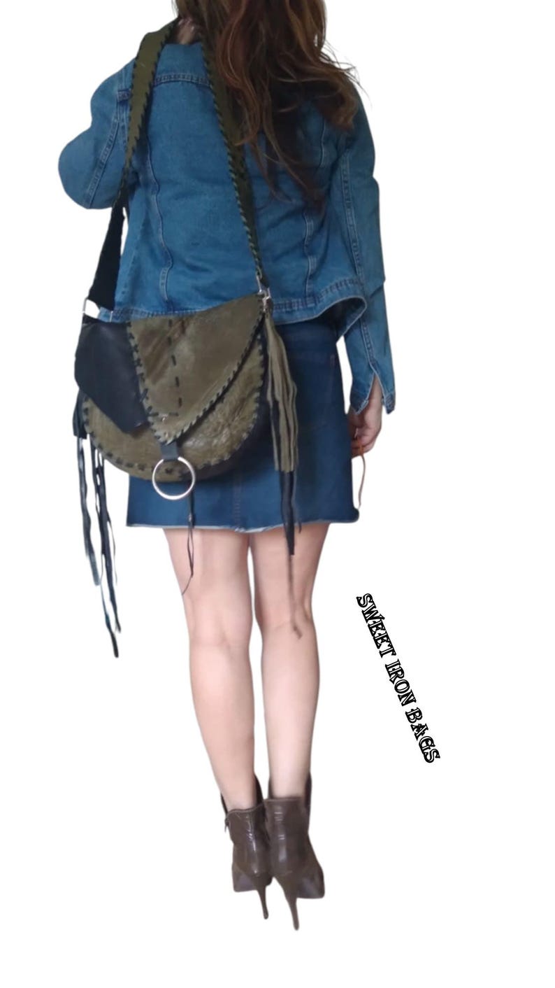 May include: A woman wearing a denim jacket and a short denim skirt is carrying a green and black leather crossbody bag with fringe details. The bag has a silver ring on the front.