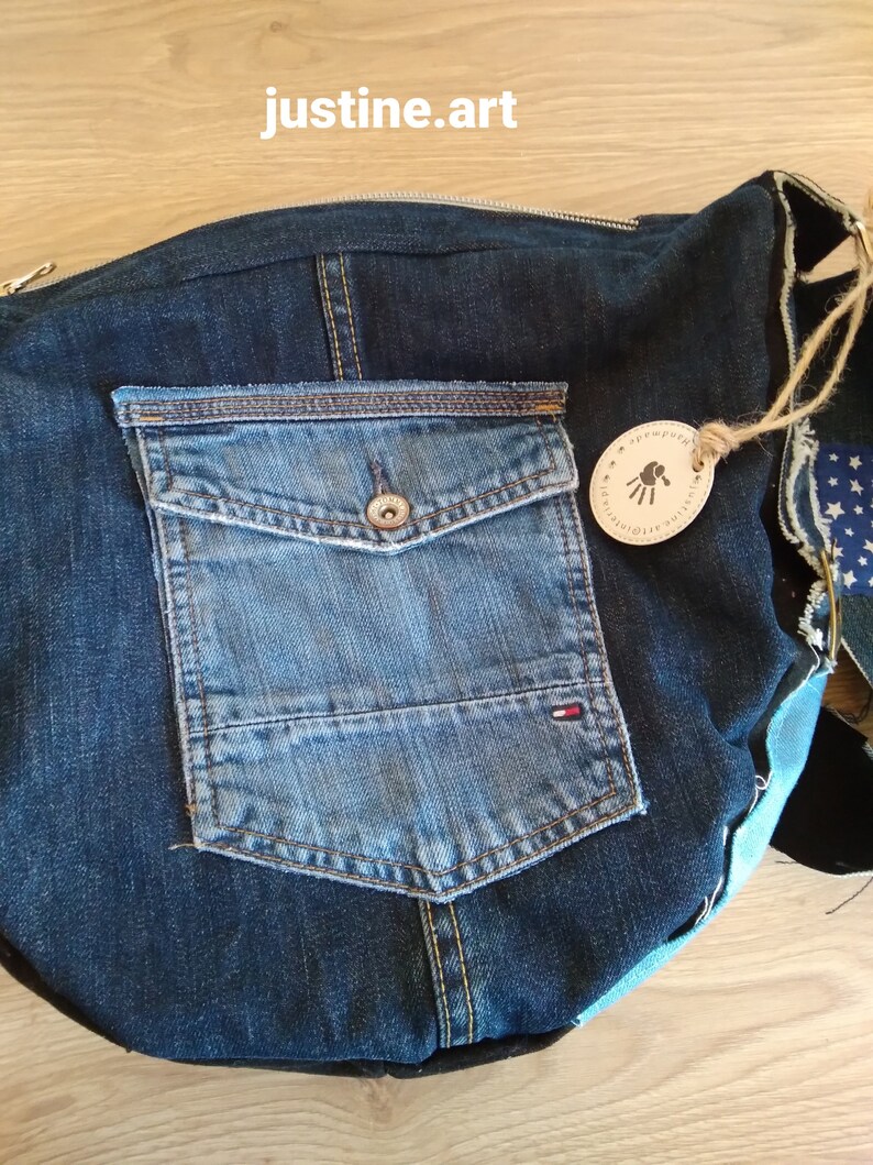 Puede incluir: Un bolso tote de mezclilla azul con un bolsillo grande en la parte delantera. El bolso est&aacute; hecho de materiales reciclados y tiene una etiqueta de cuero con el texto "Universo Etico" y una huella de mano.