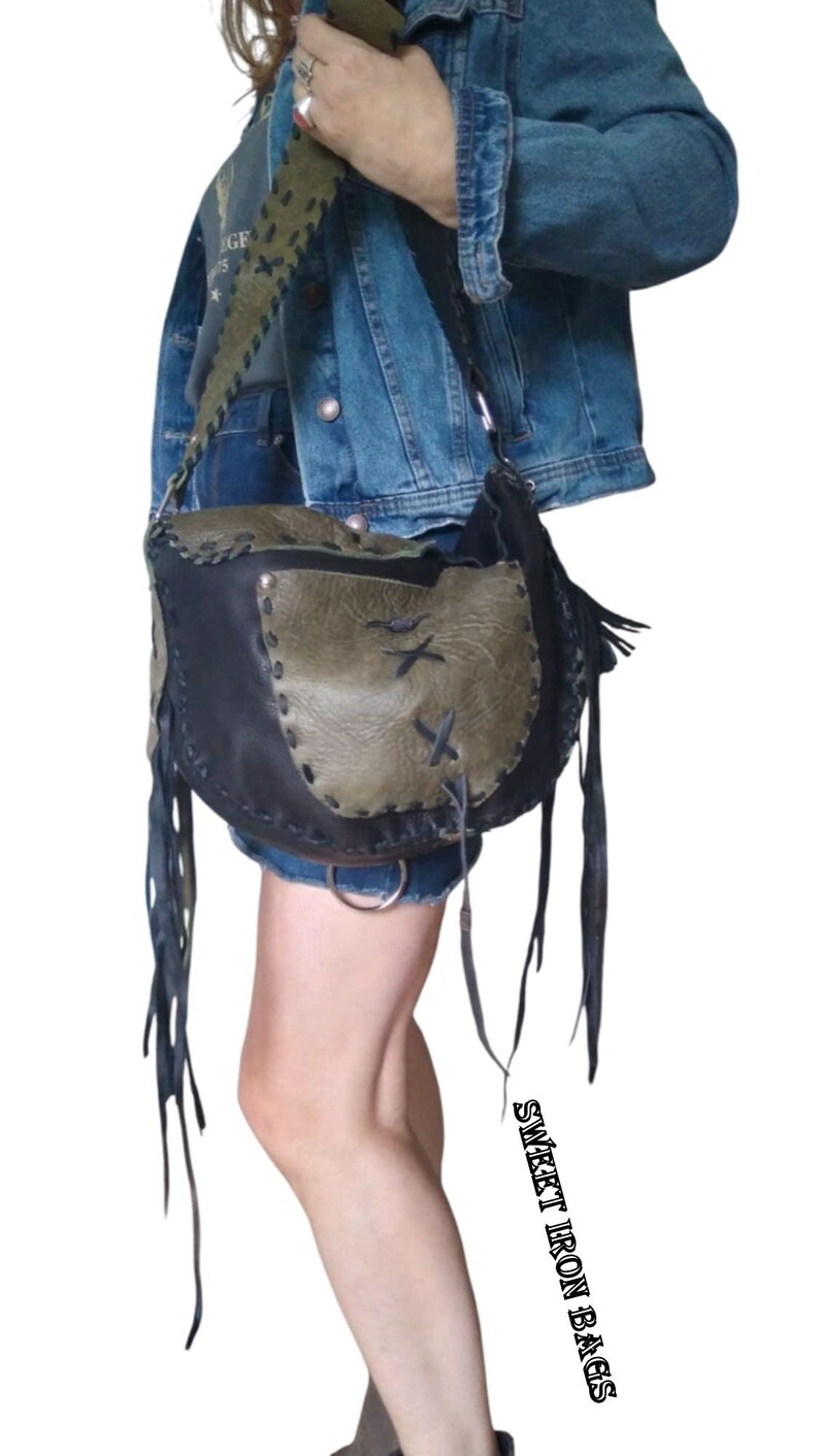 May include: A black and green leather shoulder bag with fringe details. The bag has a flap closure and a strap that can be adjusted. The bag is worn by a person wearing a denim jacket.