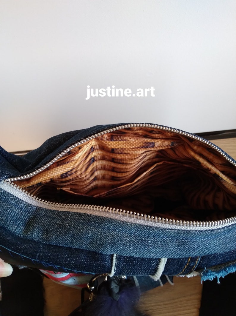 Puede incluir: Un bolso bandolera de mezclilla azul con cierre de cremallera y forro estampado en marr&oacute;n y dorado. El bolso tiene un bolsillo interior con cremallera y un llavero peludo.