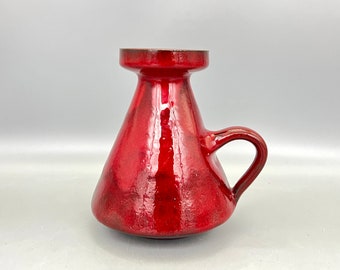 May include: A red ceramic vase with a single handle. The vase has a wide mouth and a narrow base.