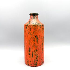 Può includere: Un vaso cilindrico in ceramica arancione con superficie strutturata e bordo scuro. Il vaso presenta macchie nere su tutto il corpo. Il vaso è alto circa 25 cm.