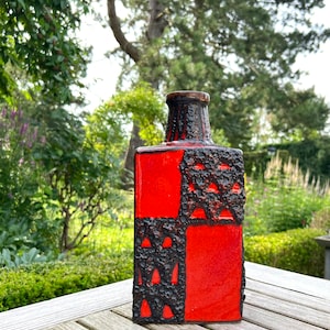 Könnte beinhalten: Eine rote und schwarze Keramikvase mit geometrischem Muster. Die Vase hat eine strukturierte Oberfläche und eine quadratische Form.