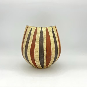 May include: A decorative, egg-shaped vase with vertical stripes in gold, dark brown, and reddish-orange. The vase has a textured surface and a wide opening. The design is symmetrical and the vase is set against a white background.
