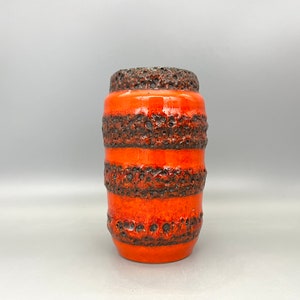 Puede incluir: Jarrón de cerámica naranja y marrón con superficie texturizada. El jarrón tiene forma cilíndrica y está decorado con bandas horizontales marrones.