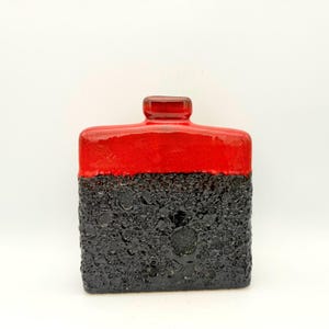 May include: A square ceramic vase featuring a two-tone design with a smooth, glossy red upper section and a textured, porous black lower section. The vessel has a small, centered neck opening at the top and a flat base for stability.