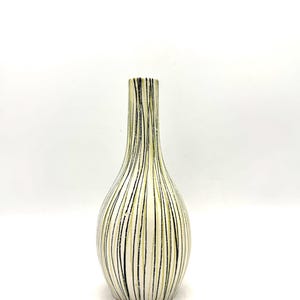 Op de afbeelding: Een slanke vaas met een crème basis en verticale strepen in zwart en lichtgroen. De vaas heeft een smalle hals en een afgeronde body. Geschikt voor bloemen of als decoratief stuk.