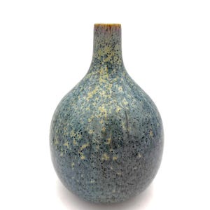 May include: A small, blue ceramic vase with a rounded body and a narrow neck. The vase has a speckled texture with yellow and black accents. The rim of the vase is a reddish-brown color. The vase is a decorative item.