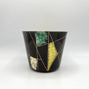 May include: A black ceramic planter with a geometric design featuring gold lines and green, yellow, and white accents.