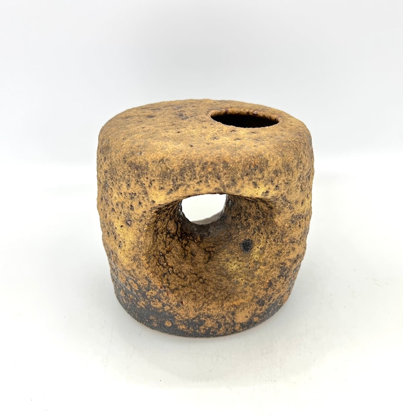 K&ouml;nnte beinhalten: Eine kleine, runde, braune Keramikvase mit rauer Textur und zwei L&ouml;chern. Die Vase hat ein rustikales, handgemachtes Aussehen.