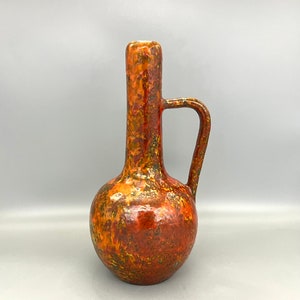 May include: A ceramic vase with a bulbous body and a long, thin neck. The vase has a mottled glaze in shades of orange, brown, and yellow.