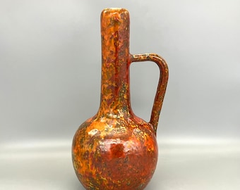 May include: A ceramic vase with a bulbous body and a long, thin neck. The vase has a mottled glaze in shades of orange, brown, and yellow.