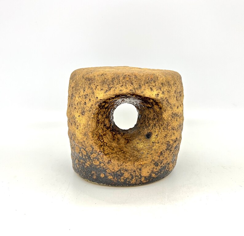 K&ouml;nnte beinhalten: Eine kleine, grob strukturierte, braune und goldene Keramikvase mit einem gro&szlig;en Loch in der Mitte. Die Vase hat ein rustikales, erdiges Aussehen.