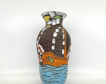 Puede incluir: Un jarrón de cerámica marrón con un diseño colorido de un barco navegando en el agua. El barco está pintado en naranja, verde y blanco, y el agua está pintada en azul. El jarrón mide aproximadamente 25 cm de alto.