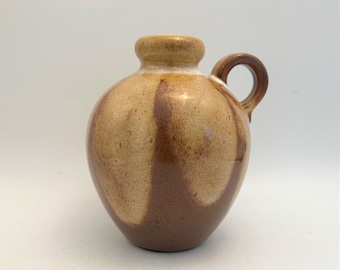 May include: A small brown and white ceramic vase with a handle. The vase has a rounded body and a slightly flared lip.