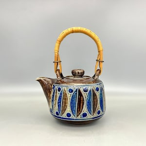 May include: A brown ceramic teapot with a blue and white geometric pattern and a woven bamboo handle.