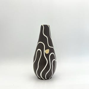 May include: A brown ceramic vase with a white abstract design. The vase has a narrow neck and a rounded body.